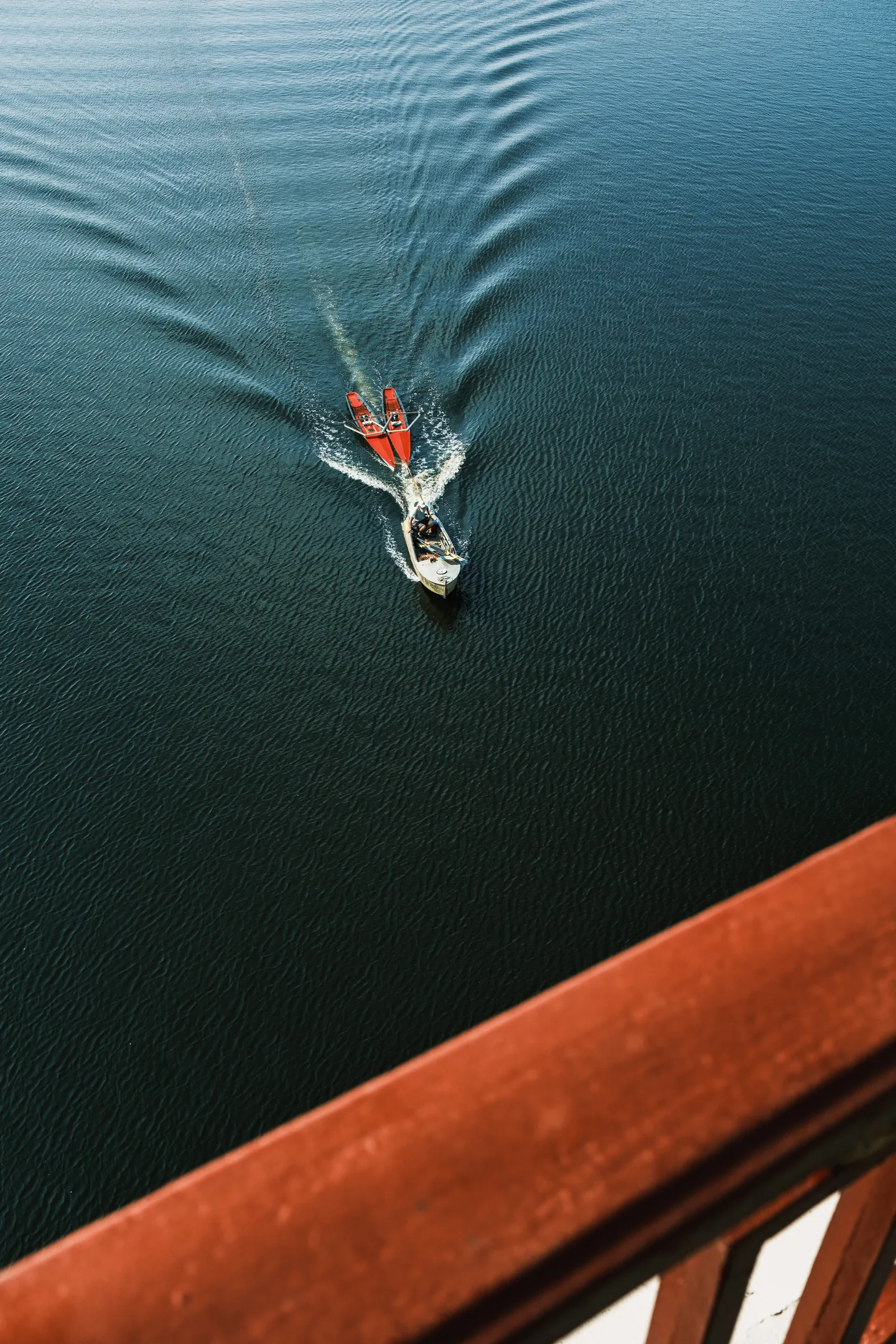 A motorboat tows a red craft beneath the bridge.