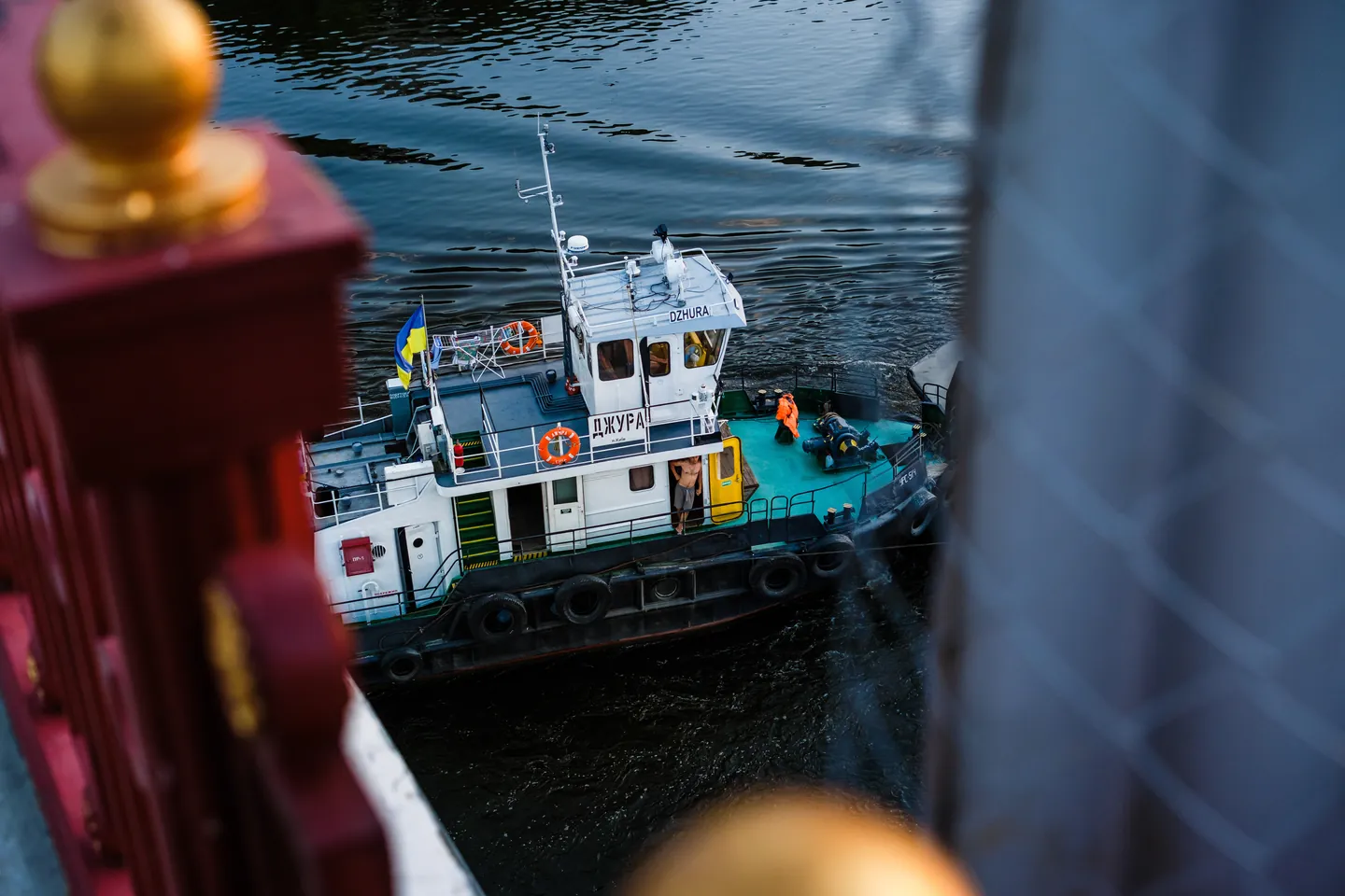 The tug Dzhura passes below the bridge, framed by its steelwork.