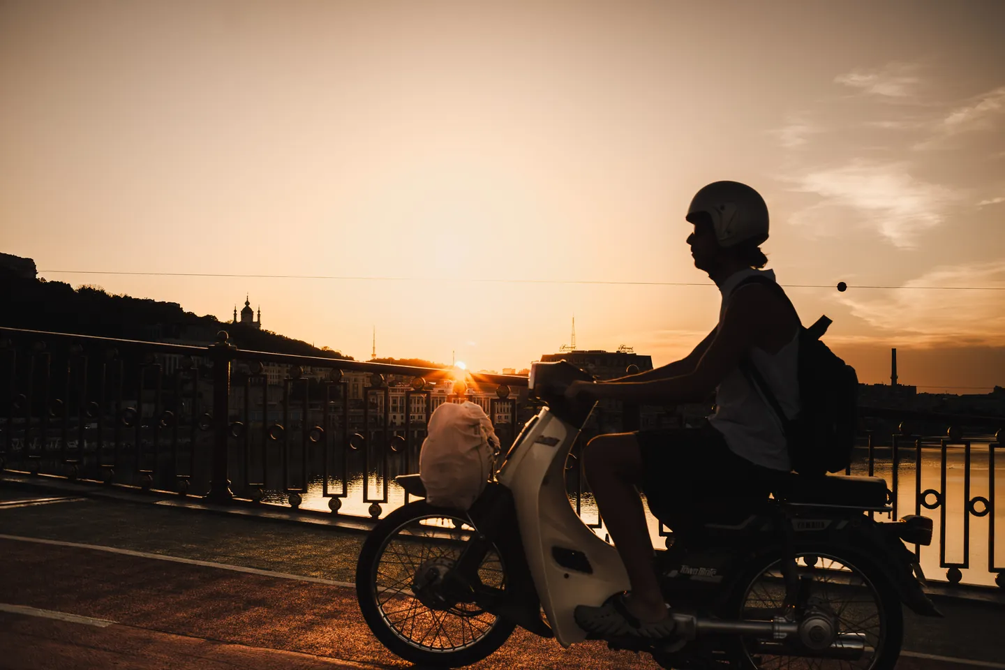 A scooter rider is silhouetted against the sunset.