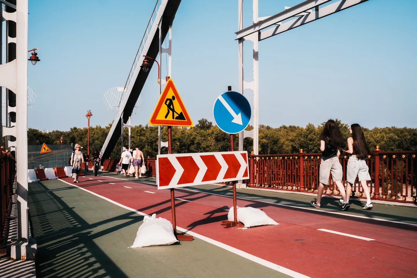 Temporary road signs stand among people walking across the bridge.