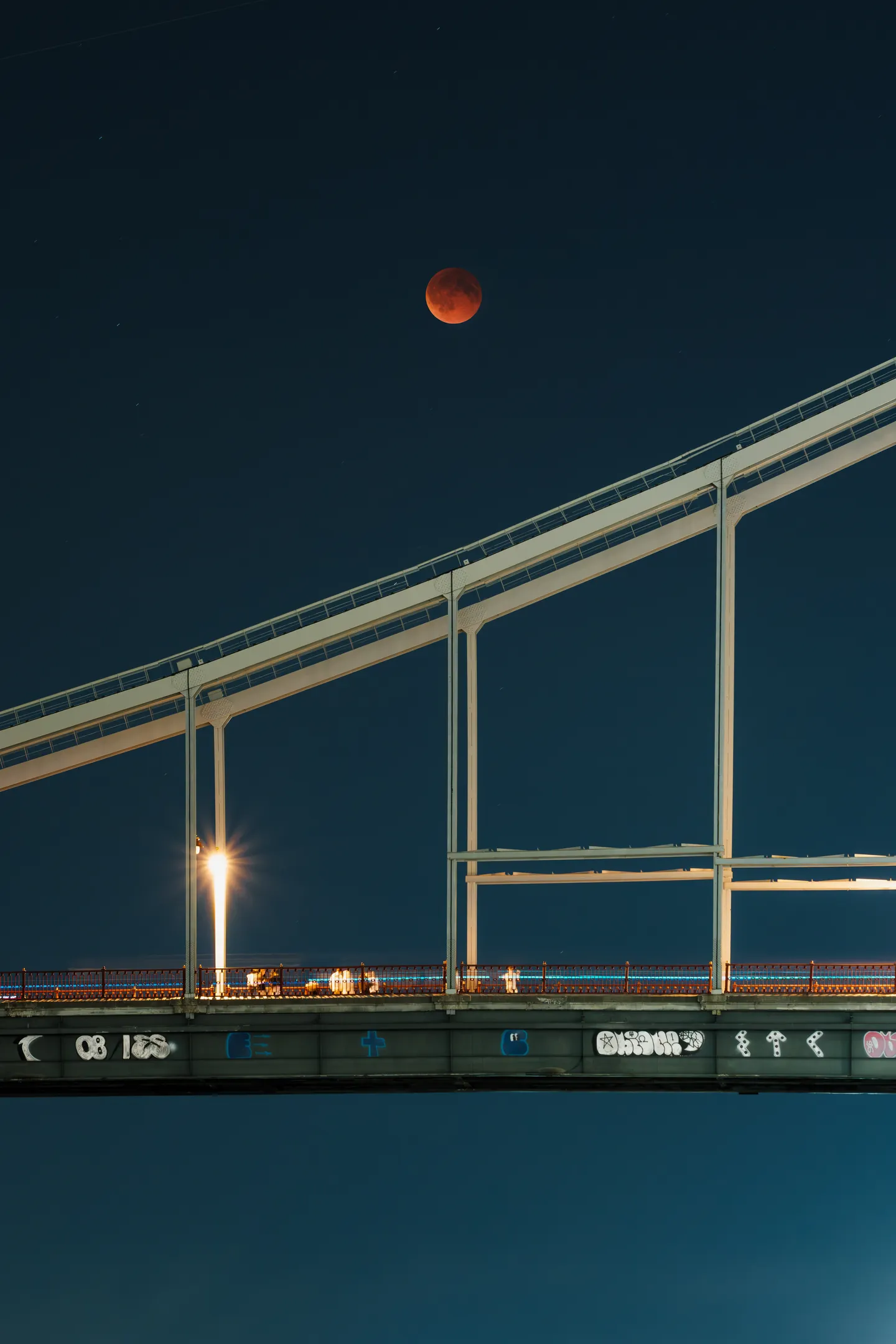 An eclipsed Moon above the bridge at night; a composite using the Moon from another photograph.
