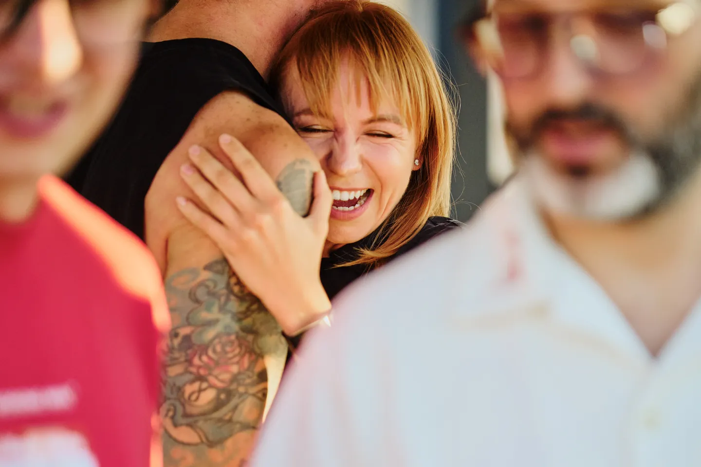 A woman laughs during an embrace, framed by people in the foreground